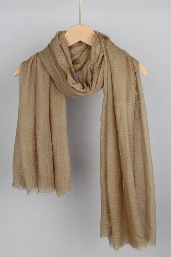 A light brown, textured scarf hangs on a wooden hanger against a plain background. The looselyboho Color-POP Scarf is loosely draped, showcasing its lightweight and soft fabric with a slightly crinkled texture, making it an ideal accessory for all-weather wear.