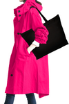 A person wearing an iconic BARBARA PINK WINDBREAKER OUTFIT by looselyboho and dark pants is carrying a large black tote bag on their shoulder. The image captures the side profile from the shoulders to the knees. The outfit, part of a limited edition collection, features buttons and a high collar.