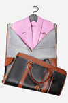 A black and brown "The Smart No-Wrinkle Foldable Travel Bag" from The Windbreaker Jacket is open, revealing a pink blazer hanging on a gray hanger inside. The bag features tan leather handles and accents, a gold zipper detail, and is made of waterproof PU leather. The light gray interior showcases the neatly packed clothing item.