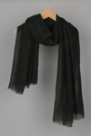 A black Color-POP Scarf with a slightly frayed texture from looselyboho is draped over a wooden hanger against a grey background. The scarf has a light, airy appearance, making it perfect for pairing with Wjackets in any season.