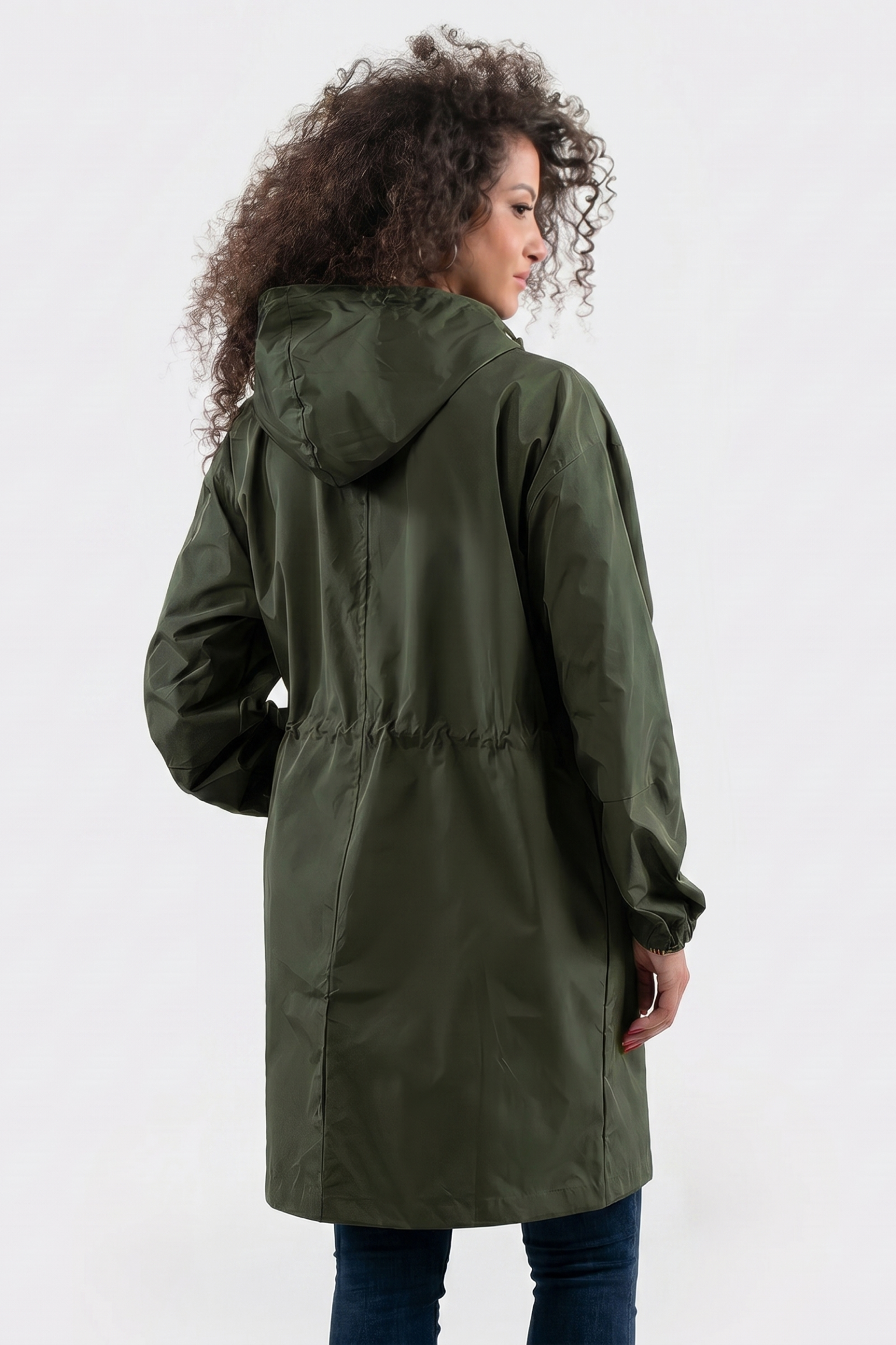 A person with curly hair is wearing The Water Resistant Hooded Oversized Windbreaker Rain Jacket in olive green and blue jeans, standing with their back to the camera against a plain light background.