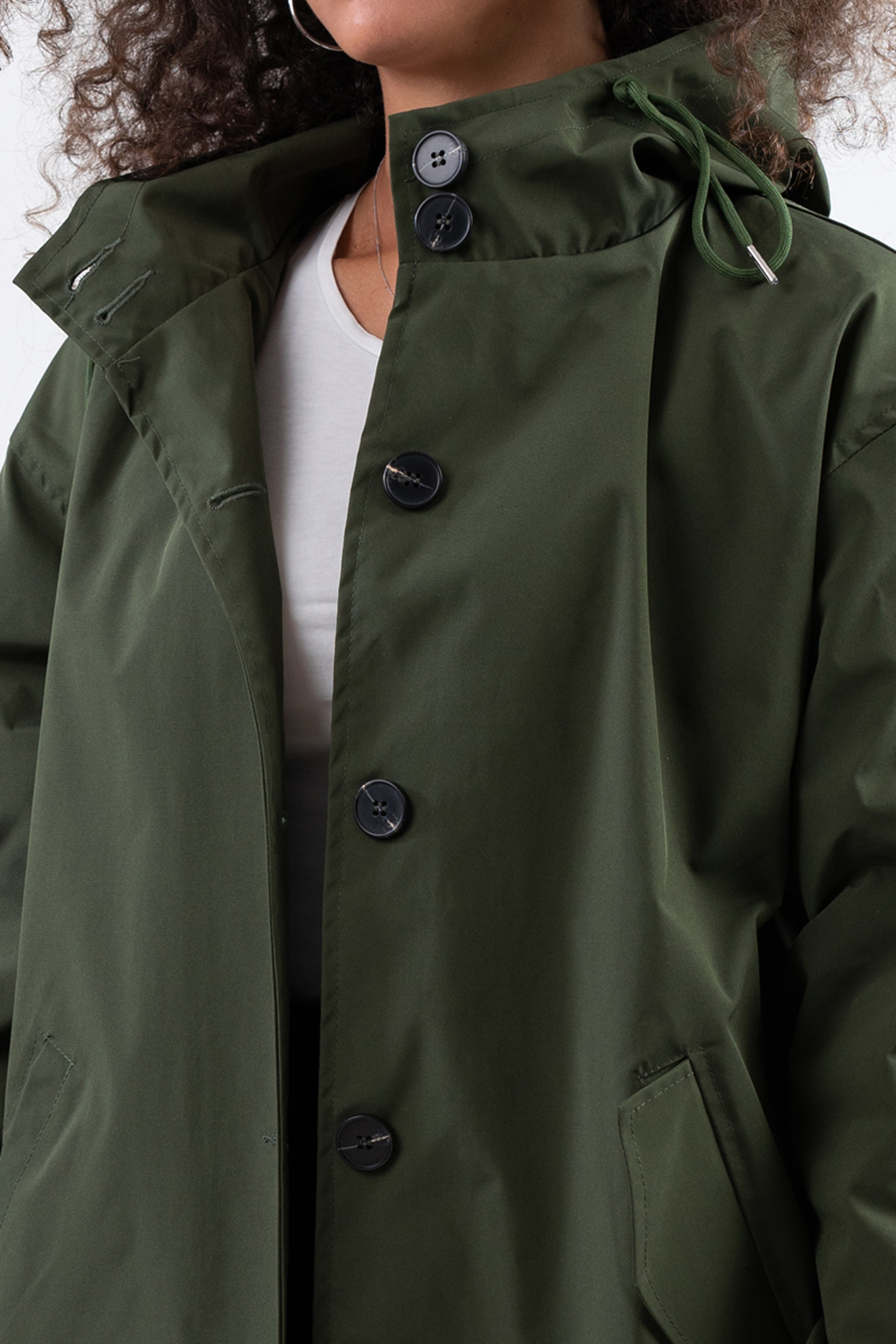 Wearing The Water Resistant Hooded Oversized Windbreaker Rain Jacket in olive green with large black buttons and a hood, the person’s white shirt, lower face, and torso are partially visible.