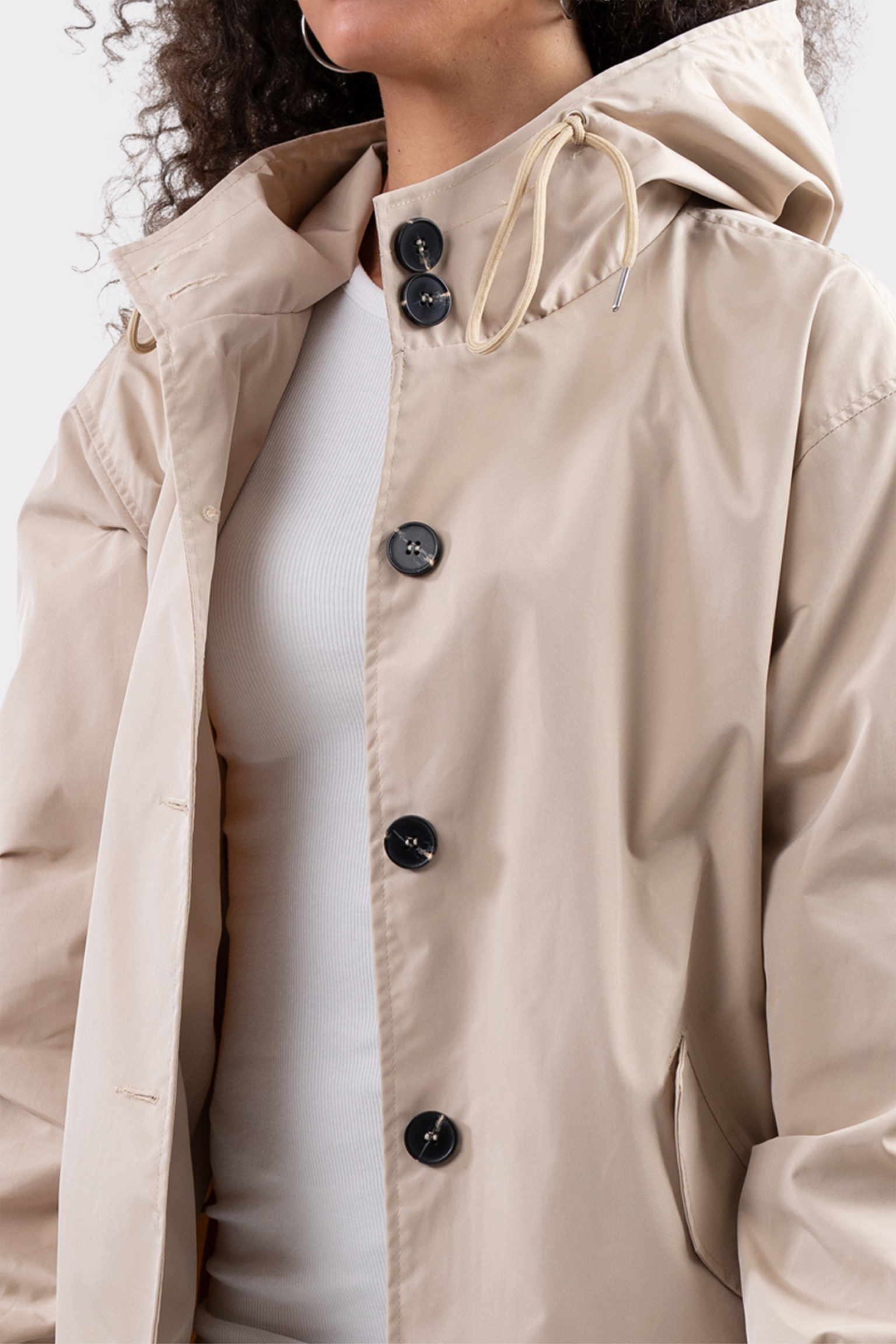 A person wears the Icon Windbreaker Rain Jacket in beige, partially unbuttoned over a white ribbed shirt, with their face partly out of frame.