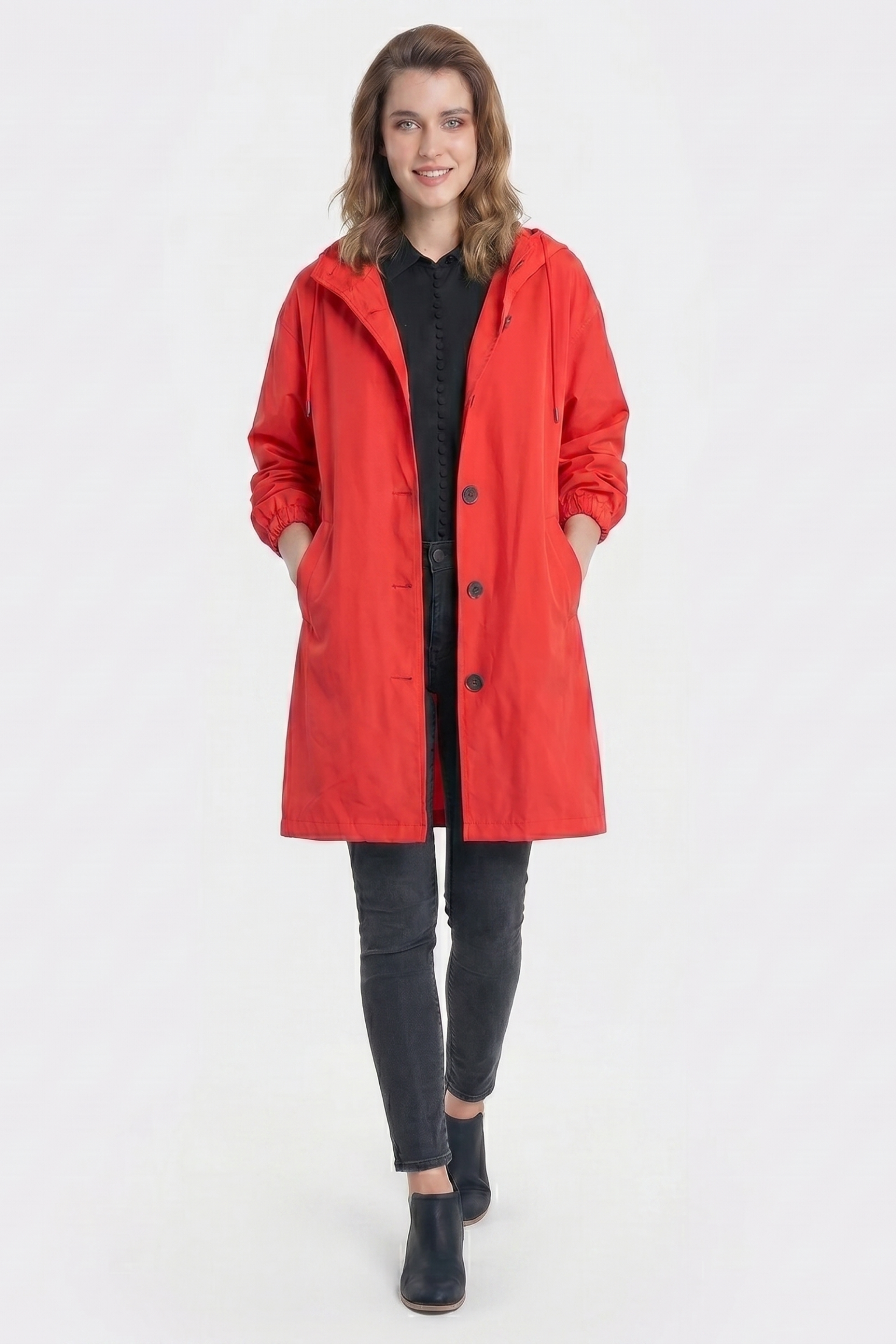 A person stands facing forward against a white background, wearing The Water Resistant Hooded Oversized Windbreaker Rain Jacket in bright red over a black shirt and pants, with hands in the pockets and black shoes.