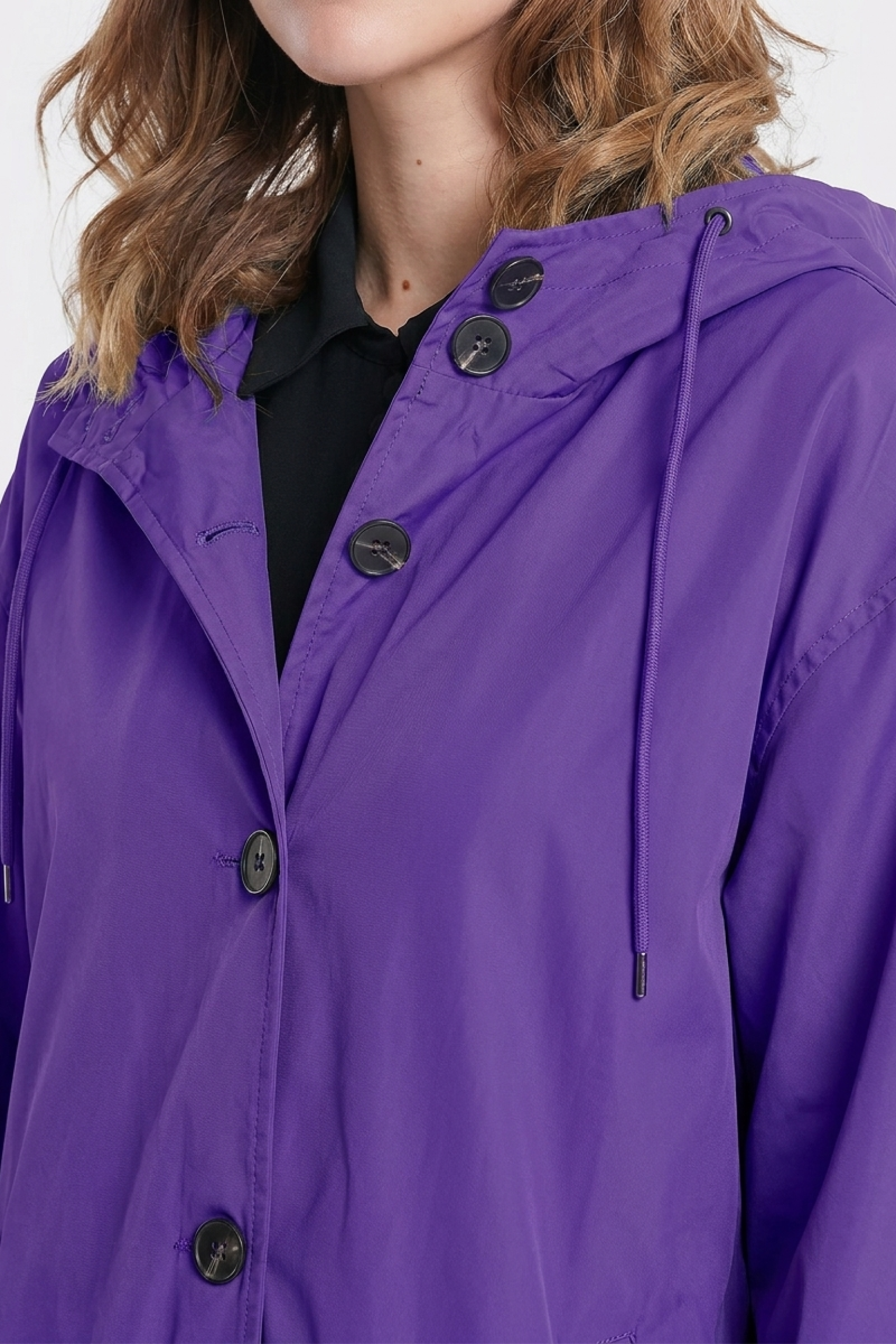 A person in The Water Resistant Hooded Oversized Windbreaker Rain Jacket, a bright purple buttoned jacket with a hood and drawstrings. Only the lower half of their face and upper body are visible; they have wavy light brown hair.
