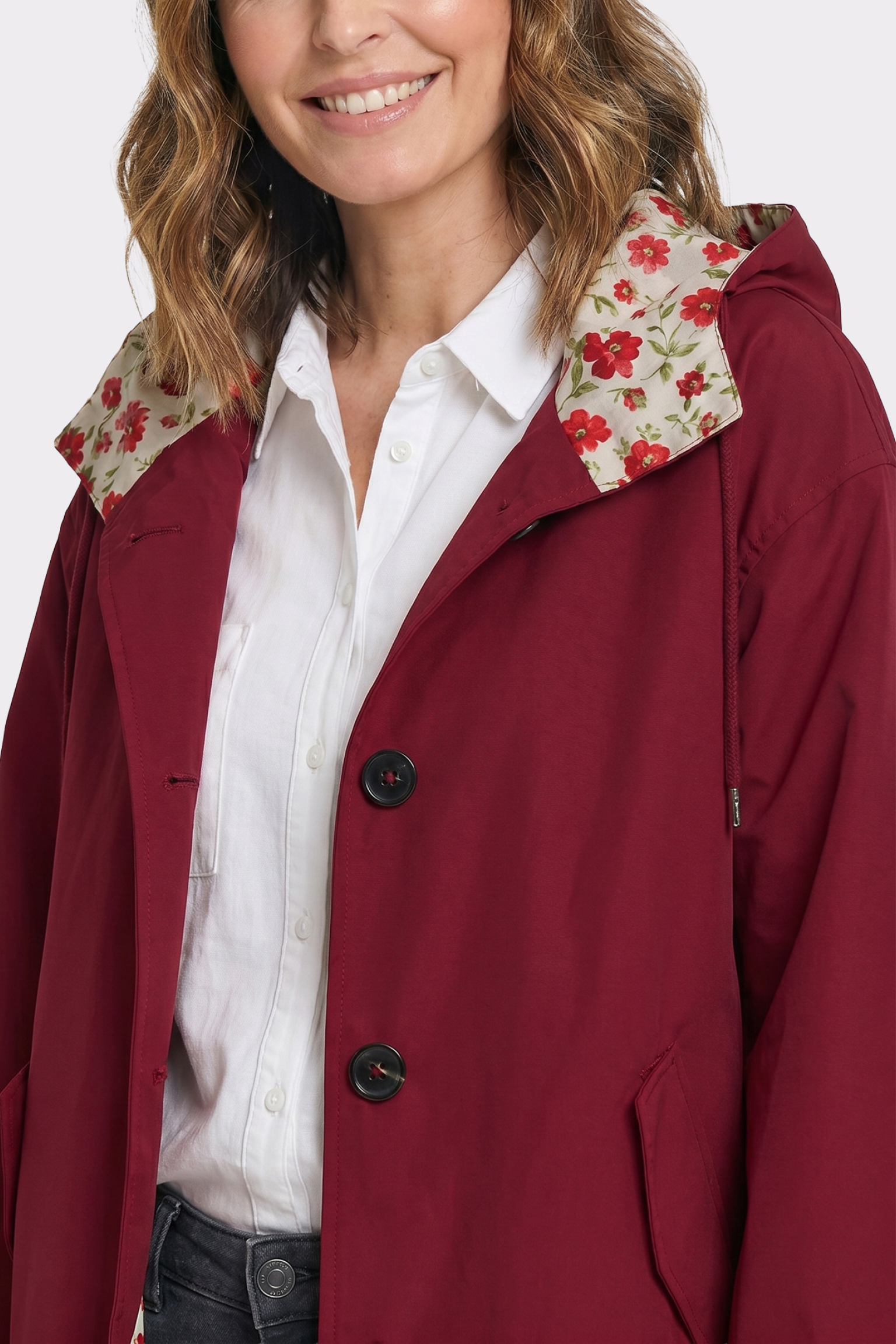 A woman models The Water Resistant Hooded Oversized Windbreaker Rain Jacket, featuring a maroon color, large buttons, and a hood lined with red and green floral fabric. Only her upper body and part of her face are shown.