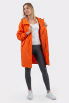 A woman faces forward in the Icon Windbreaker Rain Jacket, styled open over a white top, black leggings, and white sneakers. She holds the jacket open with one hand against a plain white background.