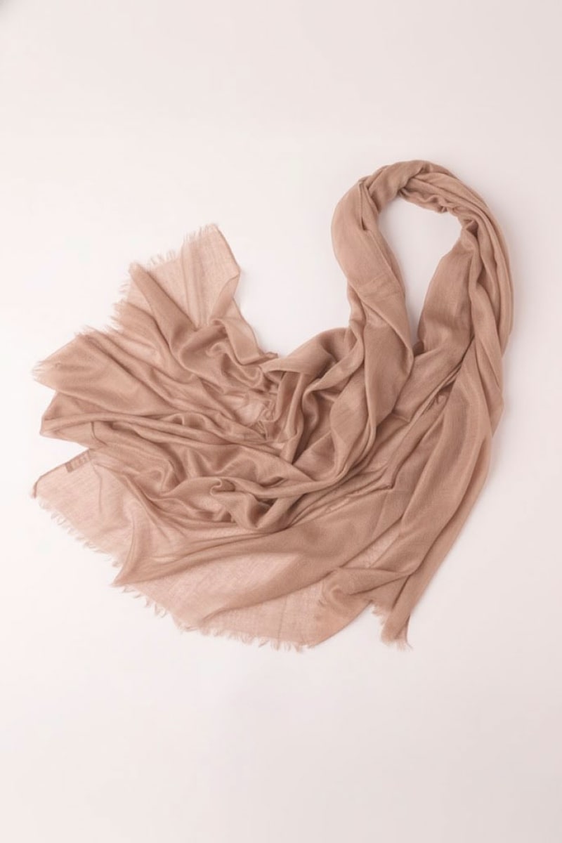 The looselyboho Sandstone Dune 100% Cashmere Scarf in light brown is spread out on a plain surface, featuring frayed edges and a soft, lightweight texture—ideal for cozy winter layering.