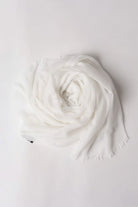 The looselyboho Ivory Whisper 100% Cashmere Scarf, a lightweight ivory accessory with subtly frayed edges, is elegantly displayed in a circular shape on a plain white background.