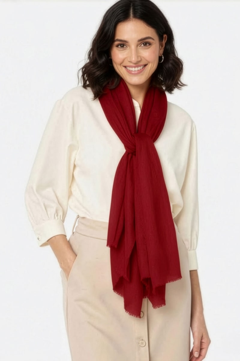 A woman with shoulder-length dark hair smiles facing forward, wearing a cream blouse, beige pants, and a loosely tied Velvet Merlot 100% Cashmere Scarf by looselyboho around her neck.