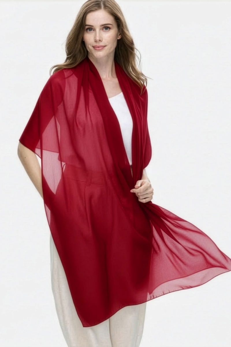 A woman with long light brown hair stands against a plain background, wearing the looselyboho Velvet Merlot 100% Cashmere Scarf over a white top and light pants, looking at the camera with a slight smile.