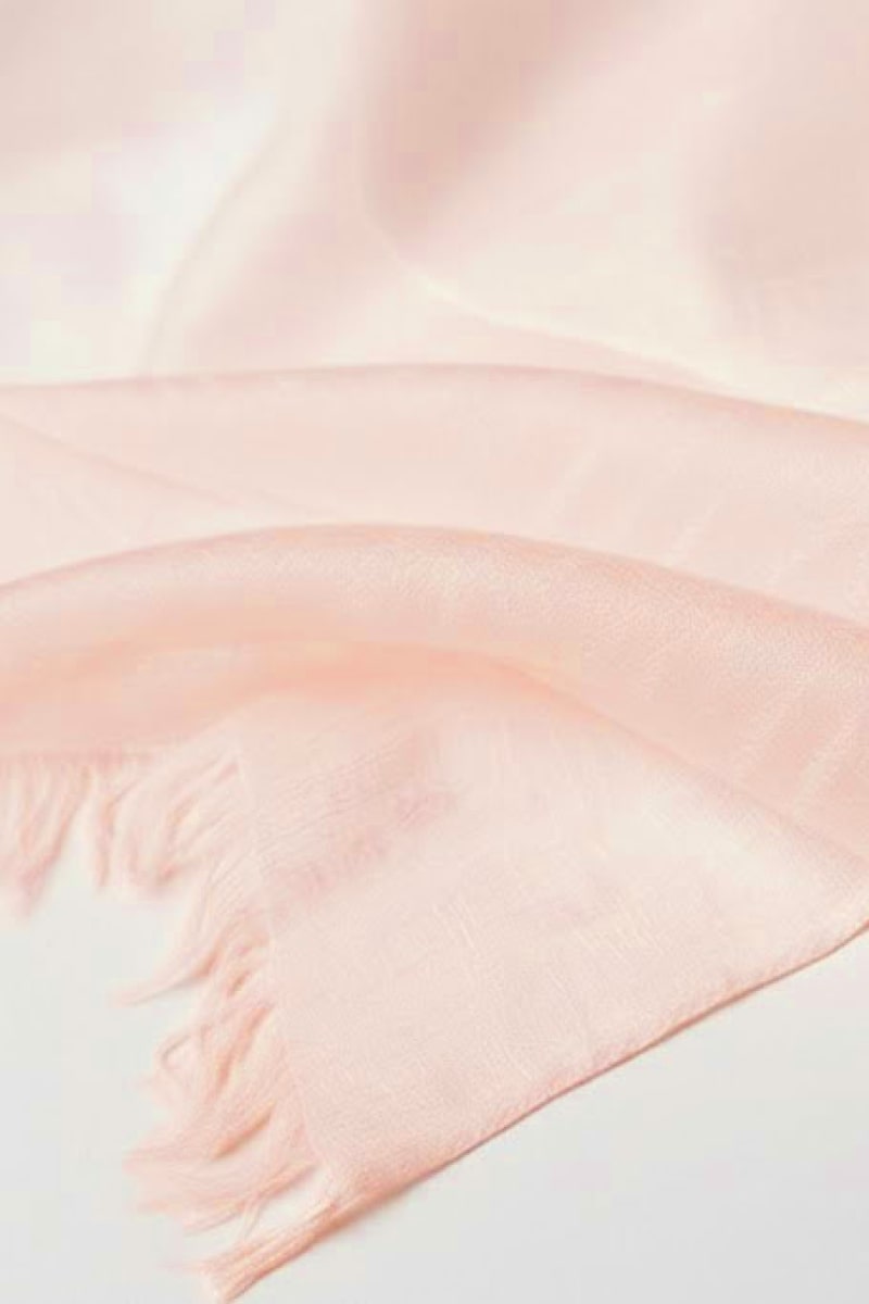 A close-up of the looselyboho Blush Rose 100% Cashmere Scarf highlights its soft, semi-sheer fabric and fringed edges, making this luxury winter accessory perfect for a touch of elegance.