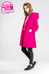 A woman stands in a gray studio wearing a bright pink hooded coat with black buttons. Crafted from lightweight water-resistant fabric, this BARBARA PINK WINDBREAKER by looselyboho pairs effortlessly with her black skinny jeans and black ankle boots. In the top left corner, there is a "Barbara Pink Limited Edition" logo.