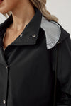 Close-up of a person wearing a black looselyboho STRIPED CARBON BLACK WINDBREAKER JACKET with snap button and zipper closure. The lightweight design is partially unzipped, revealing a striped inner lining. The person's face is not visible, and they have blonde hair.