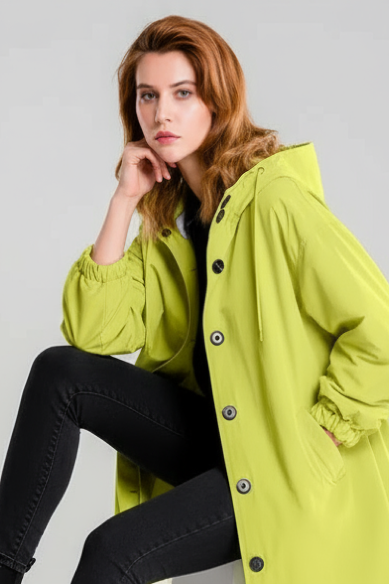 A red-haired person wears the looselyboho SUNLIT YELLOW WINDBREAKER, paired with black pants and a black top, sitting with one hand on their chin against a plain light background.